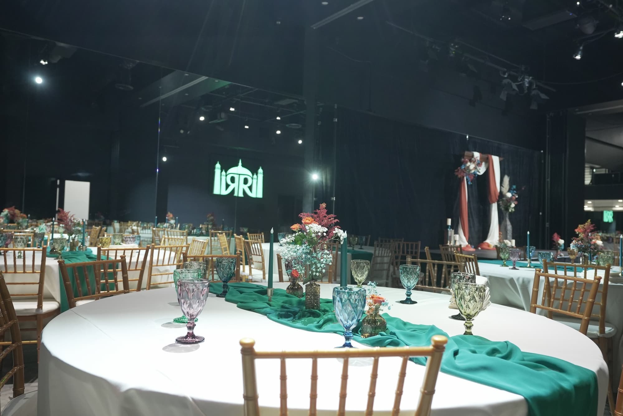 Tables with green runners, coloured glassware and a floral arch