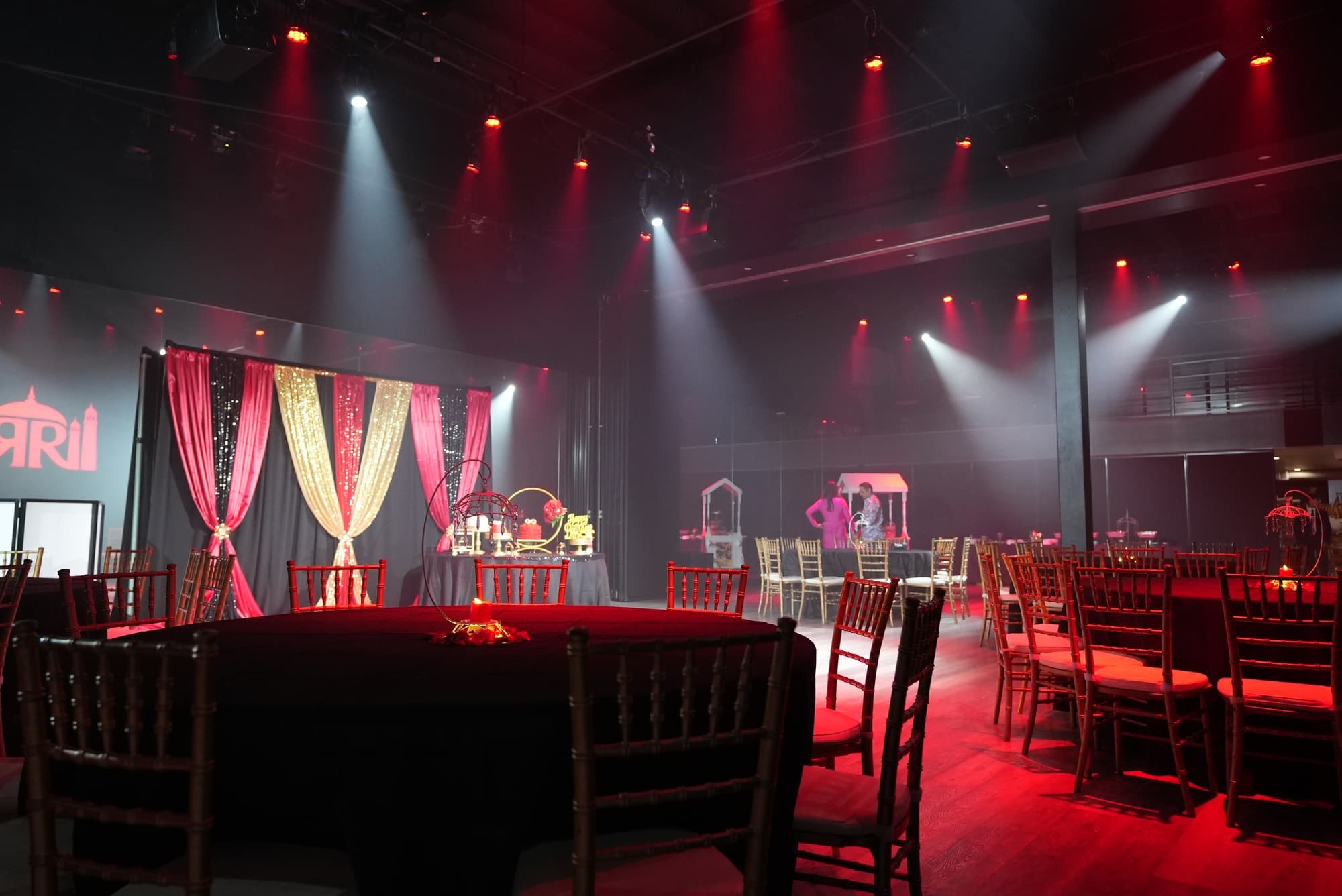 A birthday party under moving stage lights, with red and gold drapes and round tables
