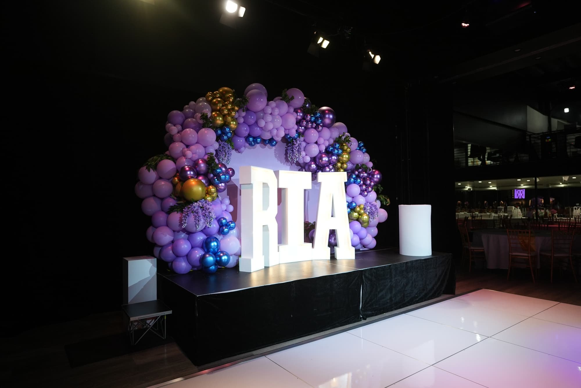 A purple and gold balloon arch with light-up letters on the stage